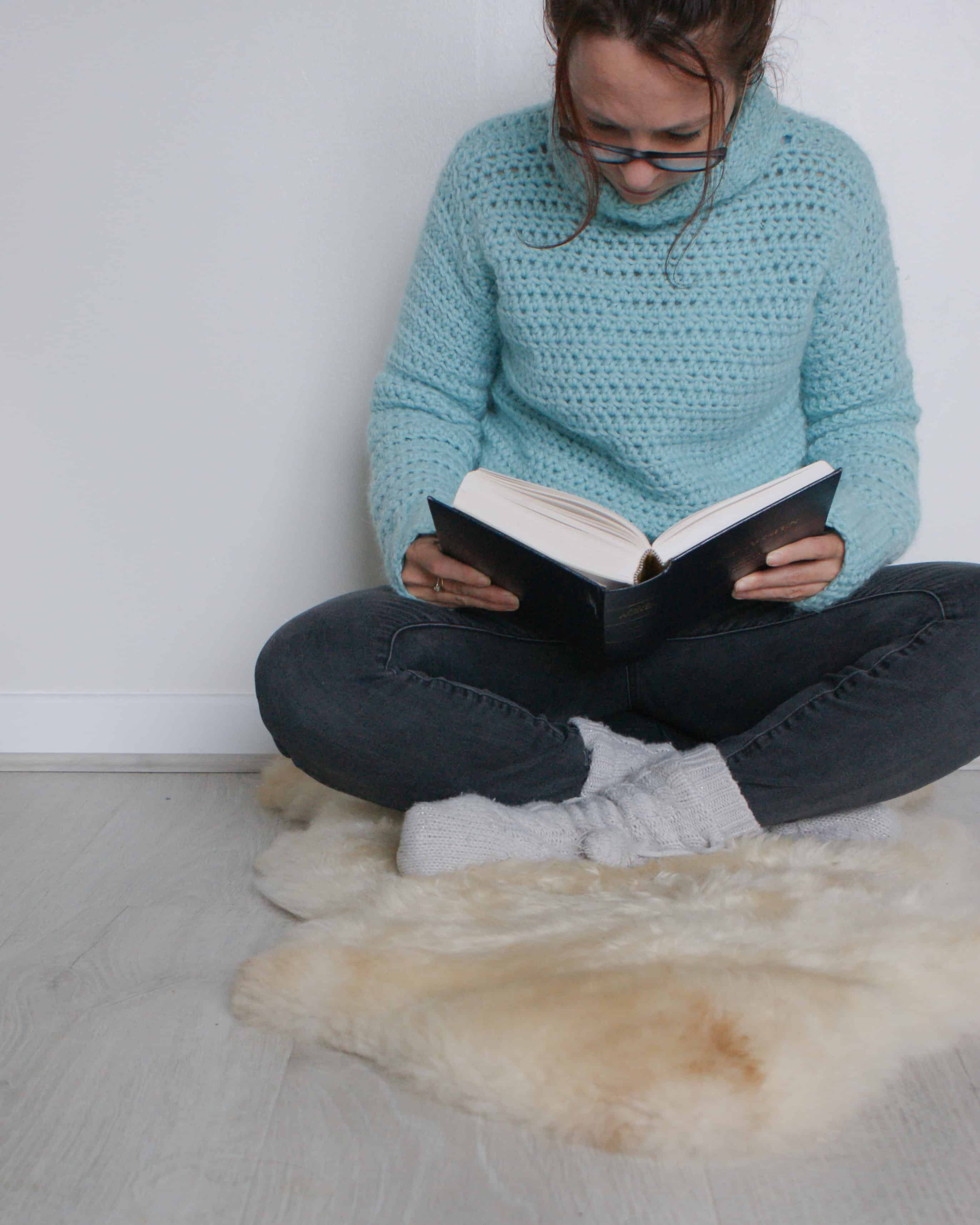 Woman crossed legged reading wearing crochet sweater