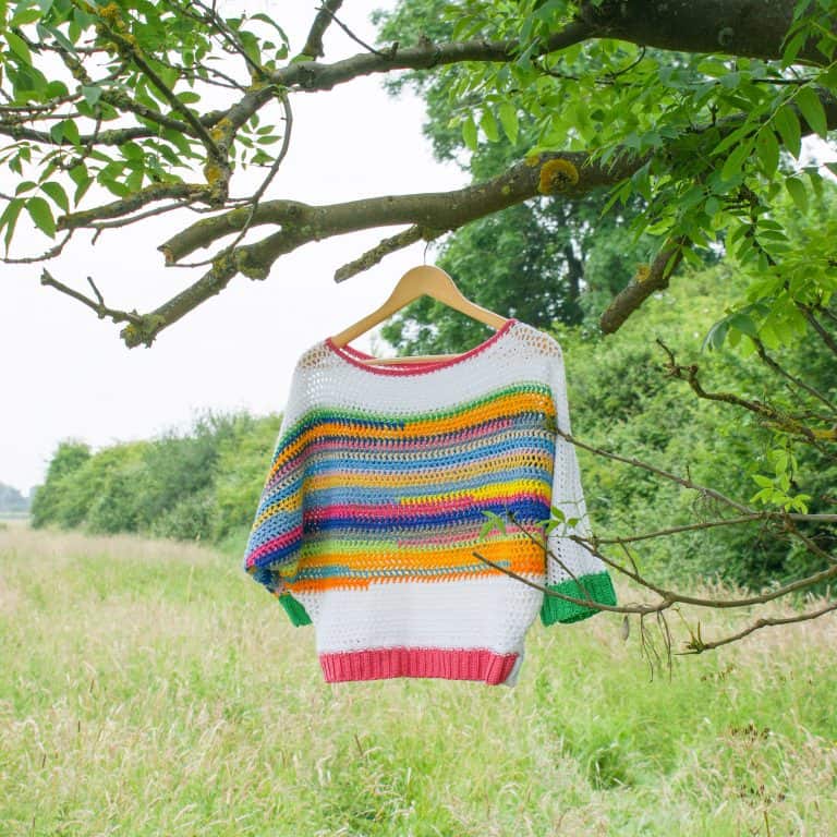 Rainbow striped crochet sweater hanging in tree in field