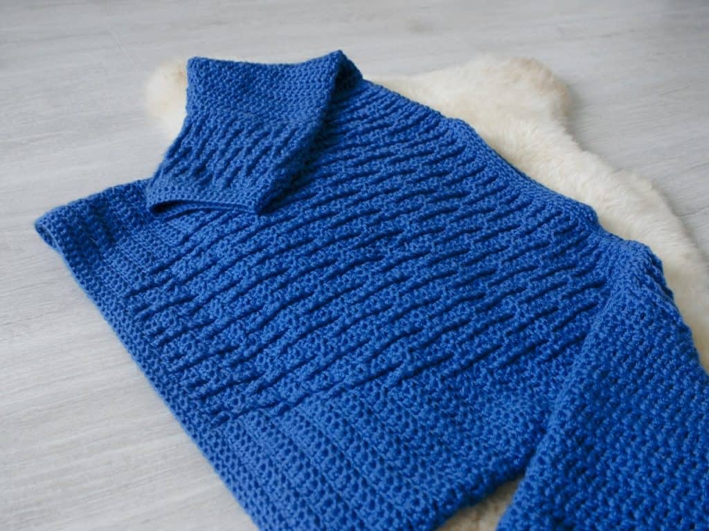 Blue textured crochet sweater on sheepskin rug on grey floor