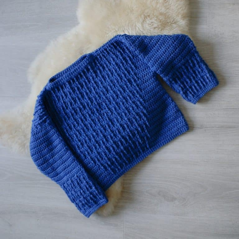 Flatlay image of blue crochet sweater on sheepskin rug