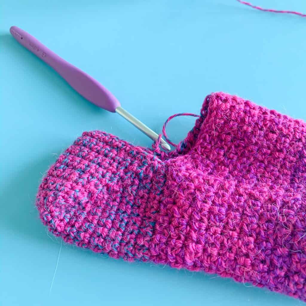 Partially made pink crochet sock on blue background