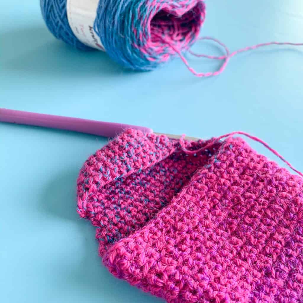Partially made pink crochet sock on blue background
