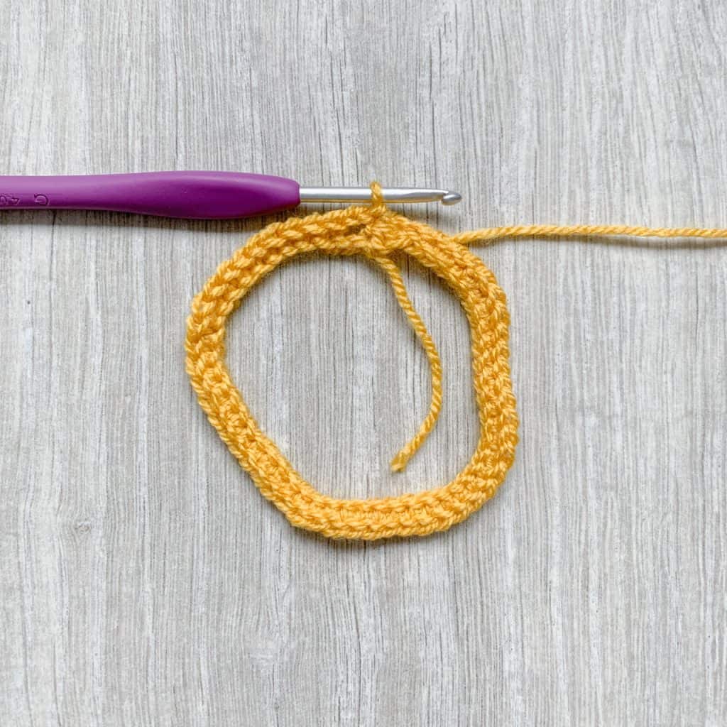 A tutorial step to make a crochet bow shows Two rounds or crochet in yellow stitches with a purple crochet hook still looped in the last stitch