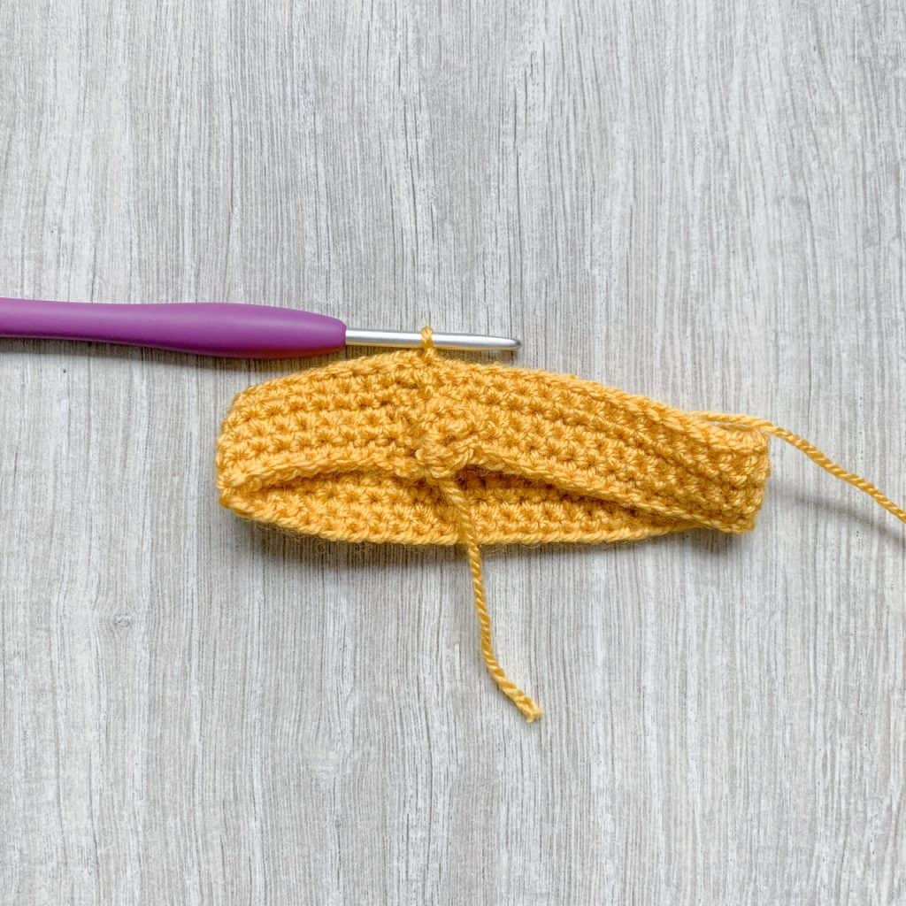 A tutorial step to make a crochet bow shows several rounds or crochet in yellow stitches