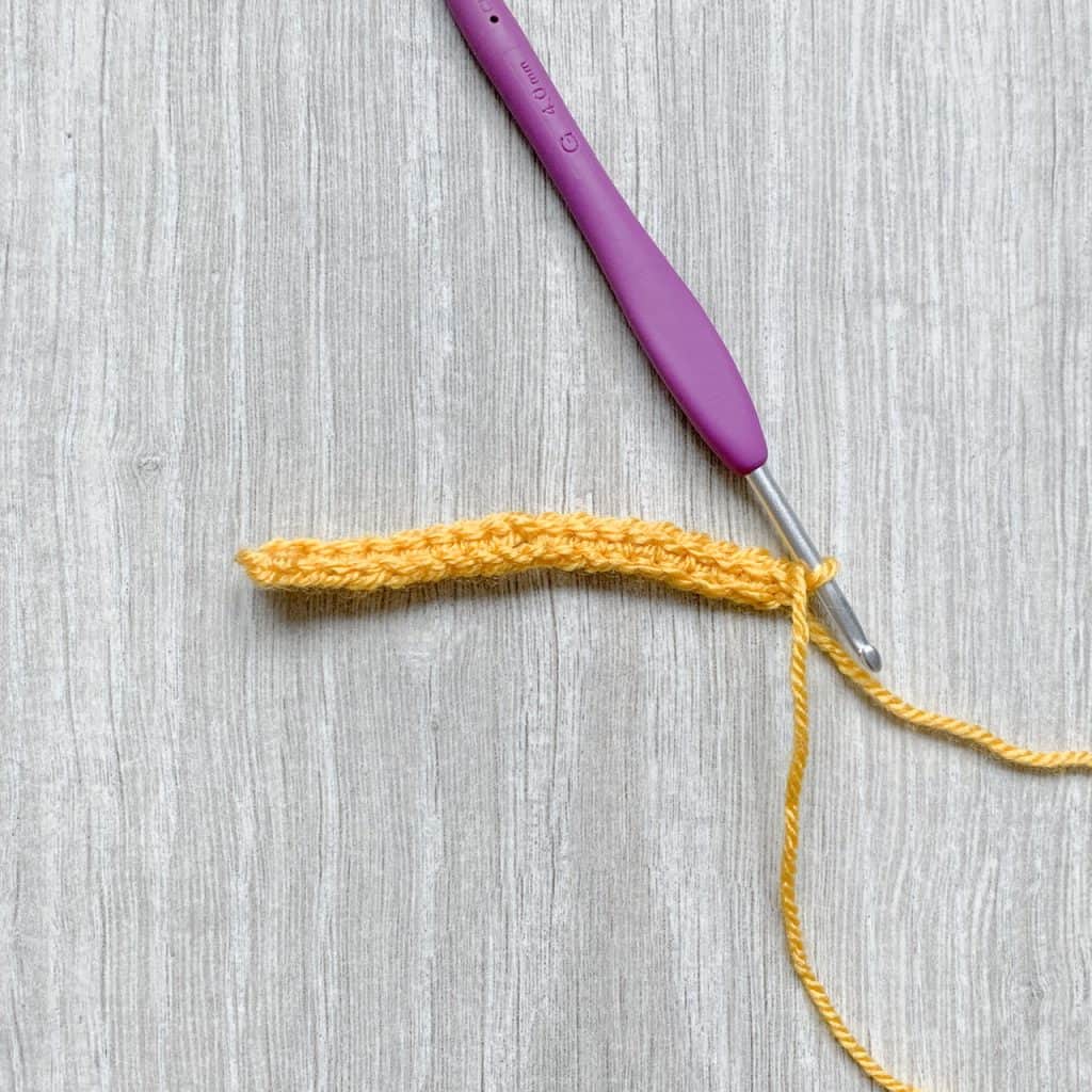 A short row of yellow crochet stitches with a purple hook still inserted into the loop of the last stitch