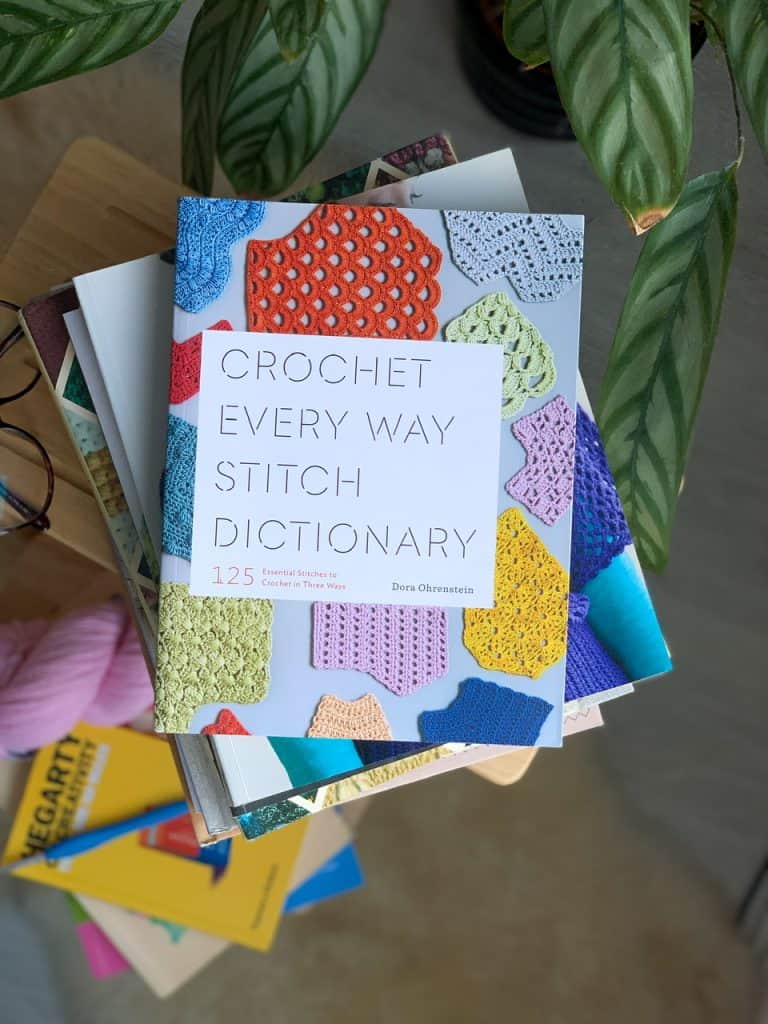 A copy of the crochet every way stitch dictionary book is seen from above on top of a pile of other crochet books