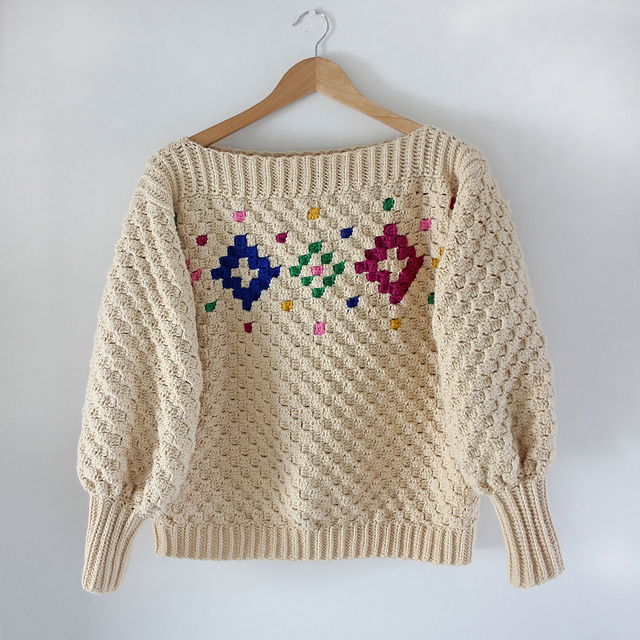 A cream corner to corner crochet sweater with speckled festive colours and shapes across the front of the sweater.