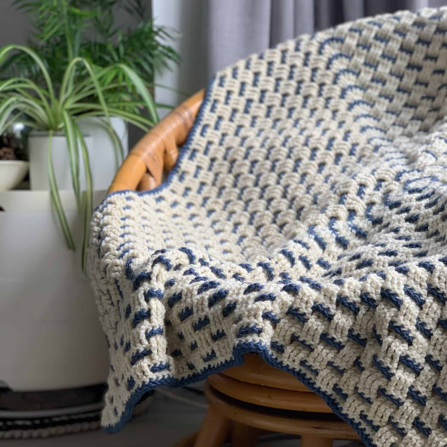 The granny weave crochet blanket is draped over a bamboo bucket chair.