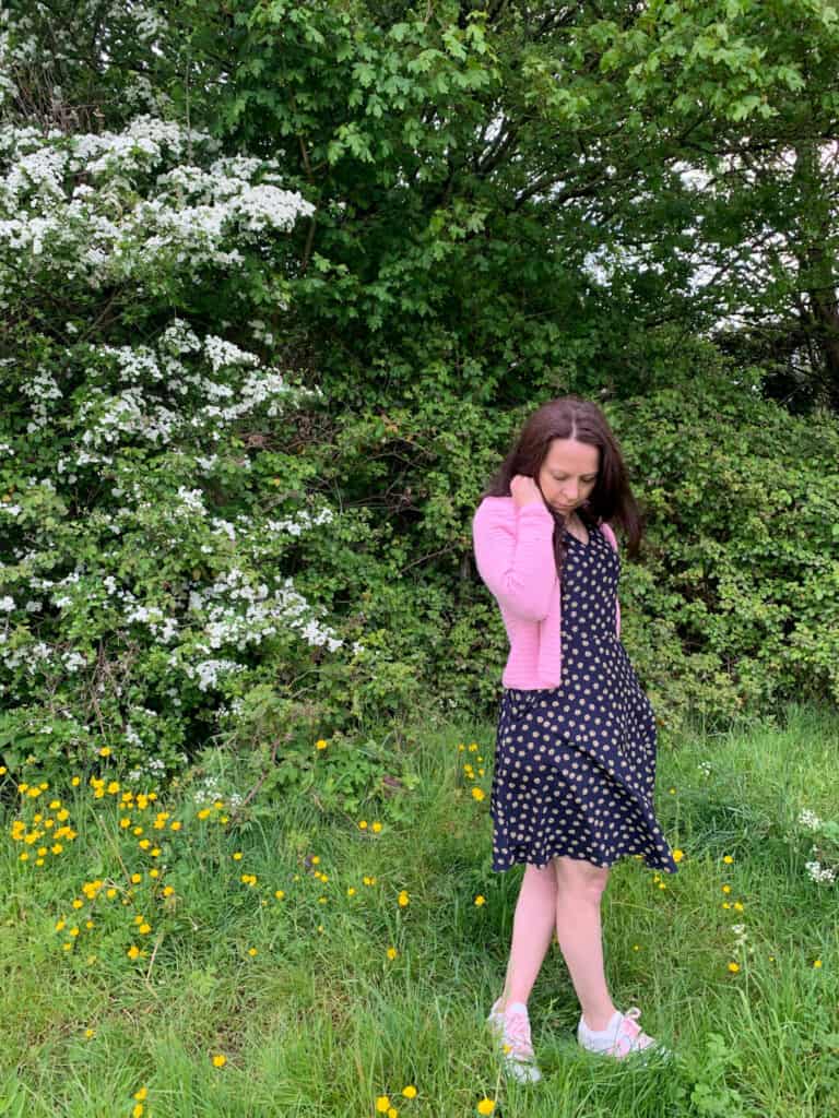 Dora wears the pink any time crochet cardigan over a navy spotted dress.
