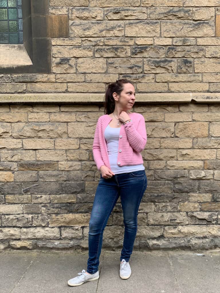 Dora stands in front of a limestone building wearing the any time crochet cardigan paired with jeans.