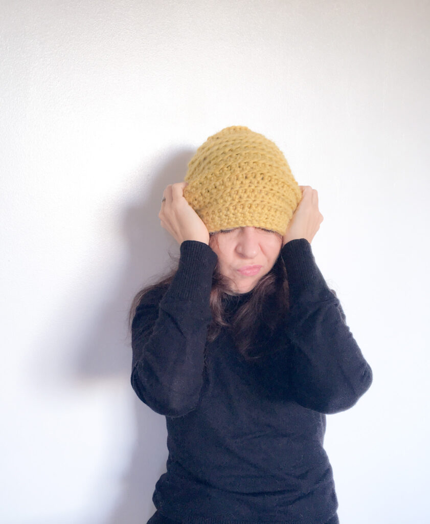 Dora pulls a yellow crochet hat over her head as she screws up her face in confusion.
