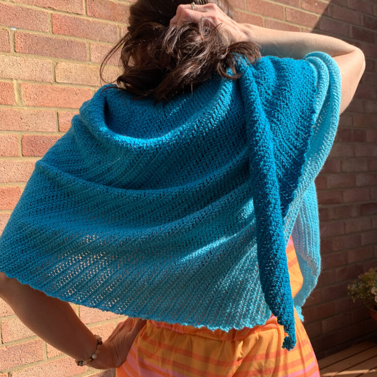 The back view of the crochet del mar asymmetric triangle shawl made in turquoise cotton blend yarn.
