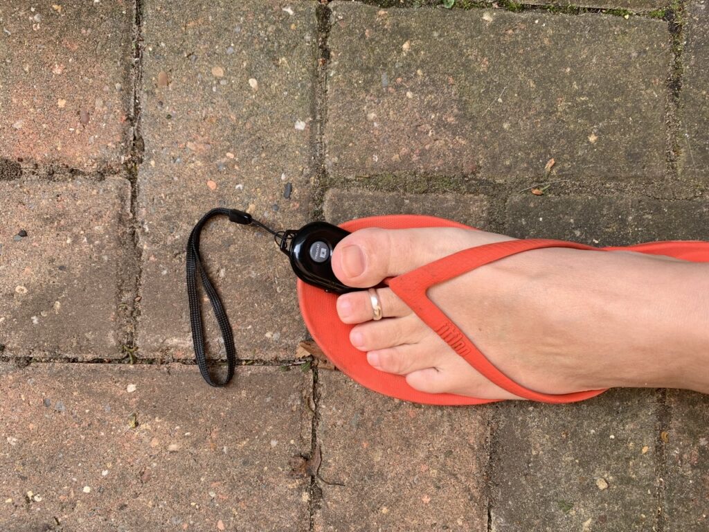 A foot in a red flip flop is seen from above clicking a camera remote with its big toe.