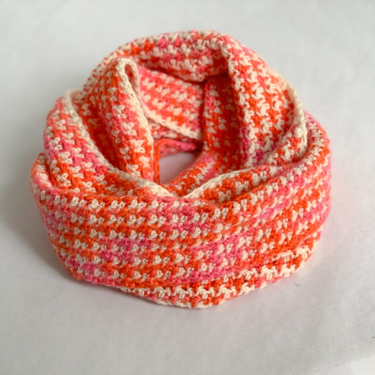 Ab orange, pink and cream dogtooth crochet infinity scarf is wrapped double and seen from the side.