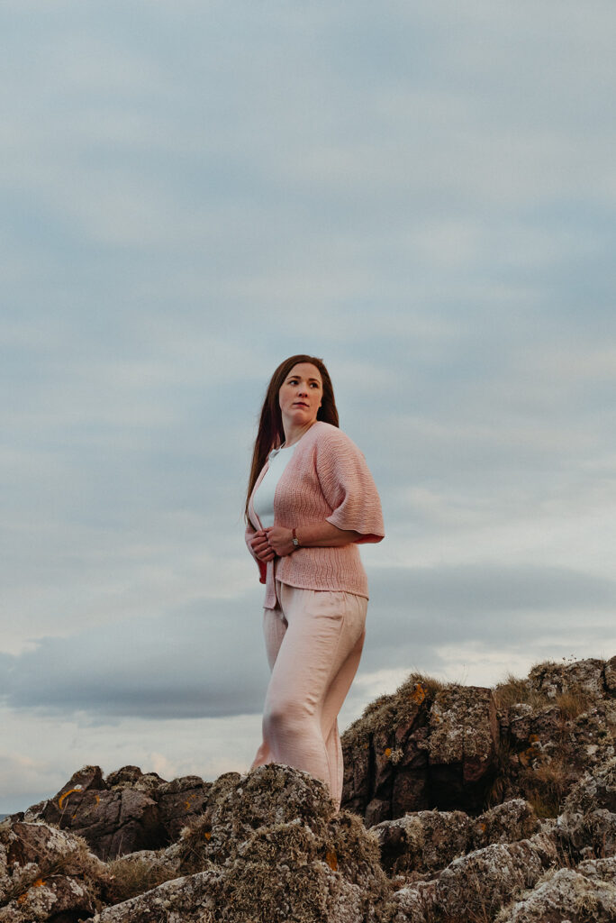 A bull length shot of a woman in pink trousers paired with the coventina crochet cardi which is an over sized mid sleeve length cardigan.