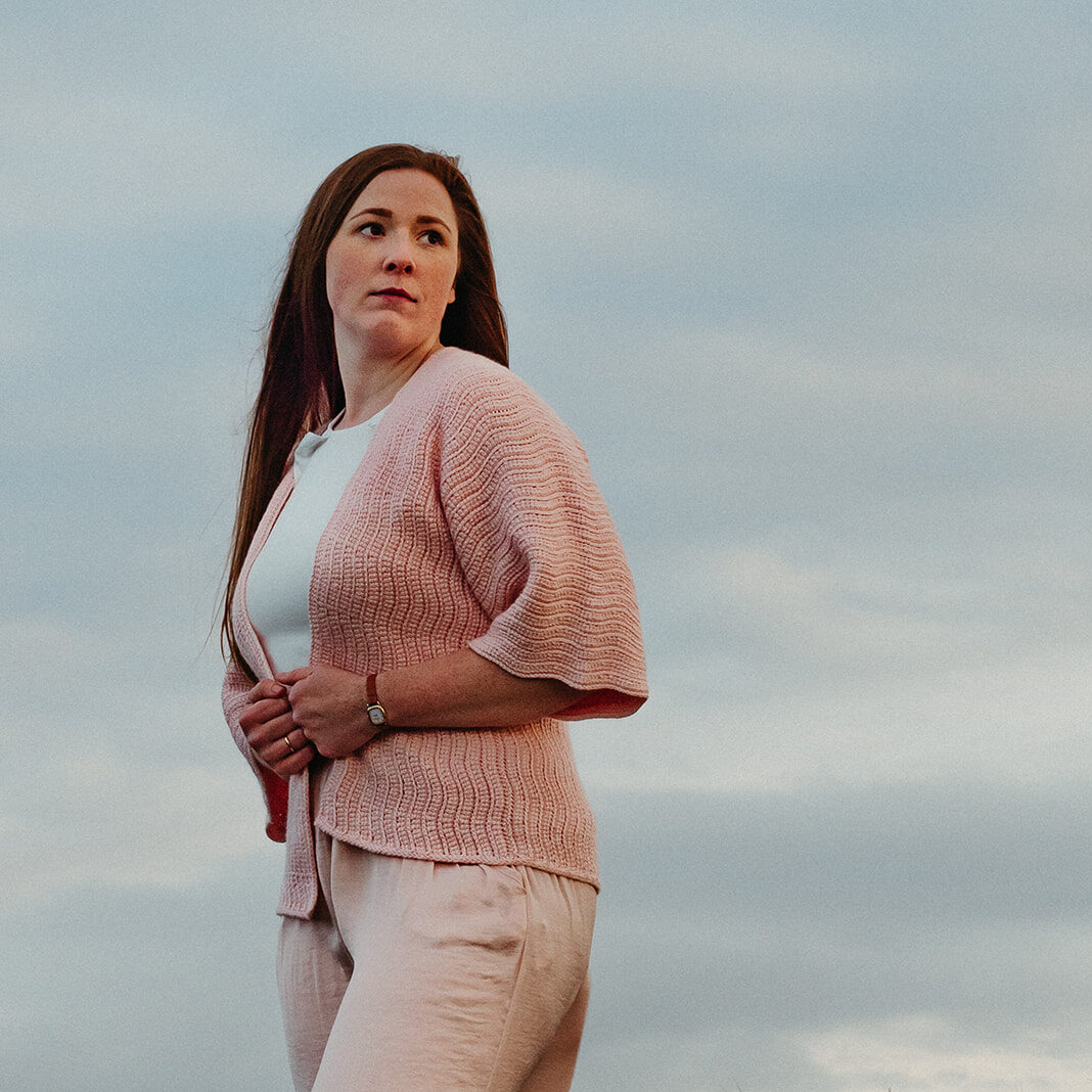 A woman wears coventina a pink crochet cardigan made with pink merino and silk yarn.