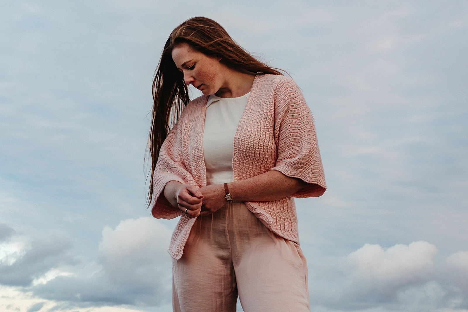 A woman wears a pink crochet cardigan with mid length sleeves and a crochet linked ripple stitch pattern.