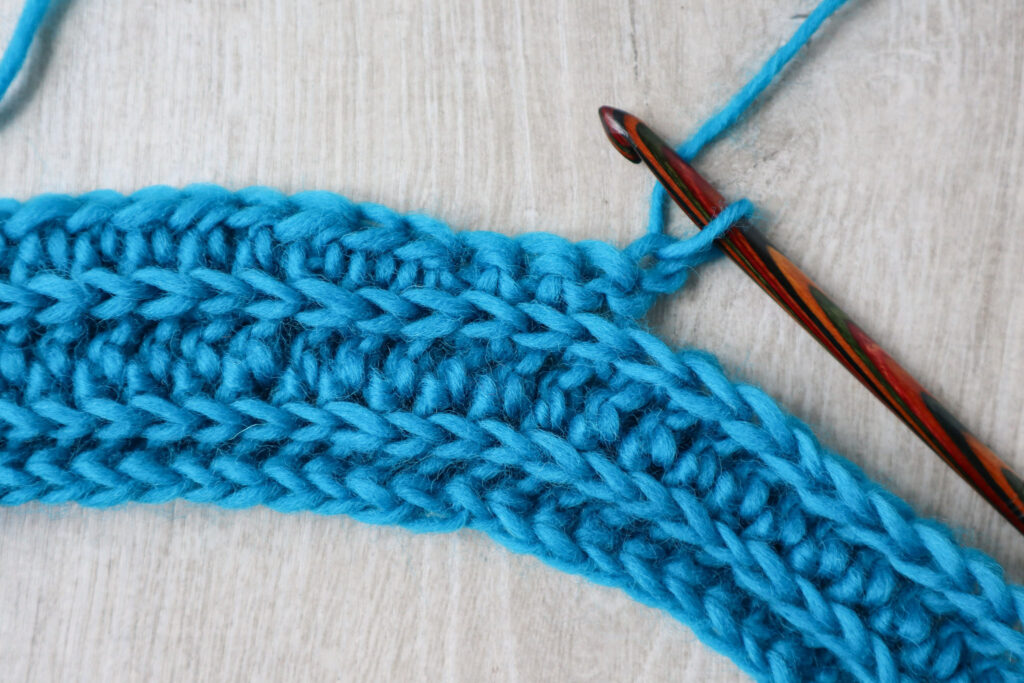 A few rows of ribbed crochet stitches with a partially worked row which is setting up for crochet short rows. The crochet hook is still attached to the swatch.