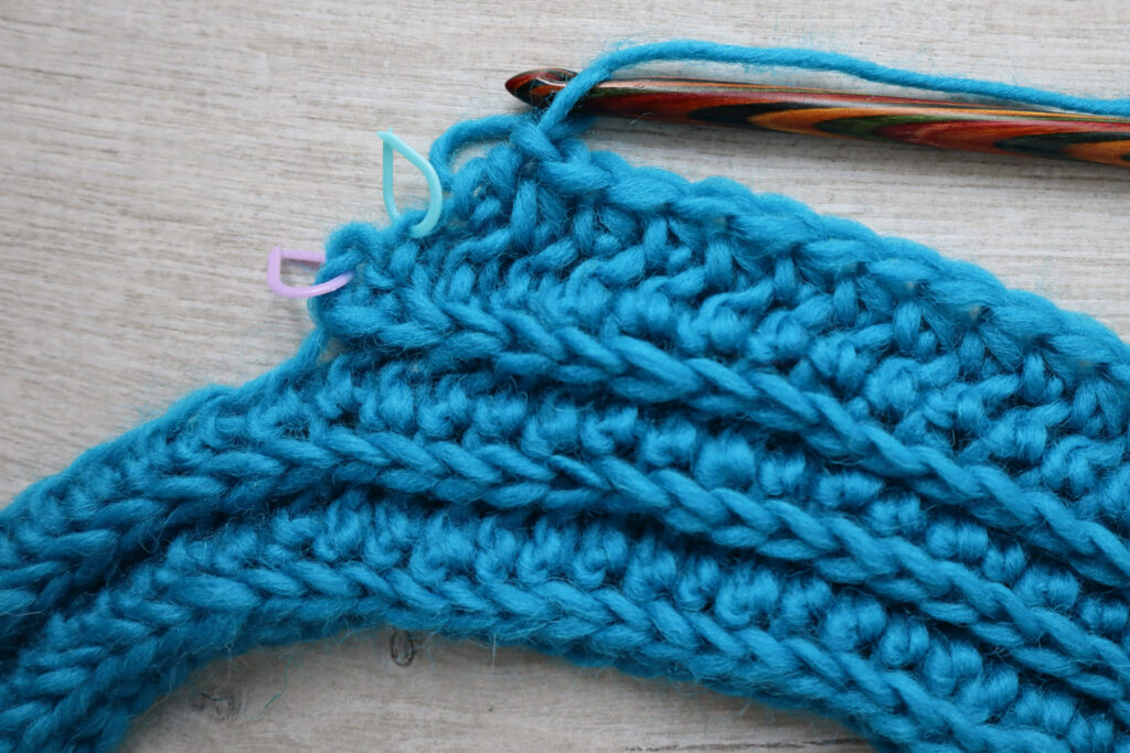 A close up of the last two stitches in a short row section, with place markers indicating where the next two stitches should be crocheted.