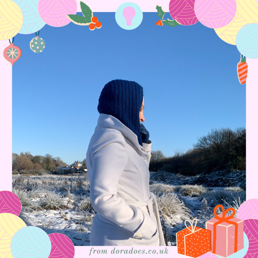 Dora seen from the side wearing a blue crochet balaclava with dora does festive graphics framing the image.