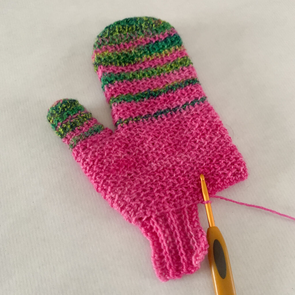 A process image of crochet ribbing in pink yarn being added to a crochet mitten.