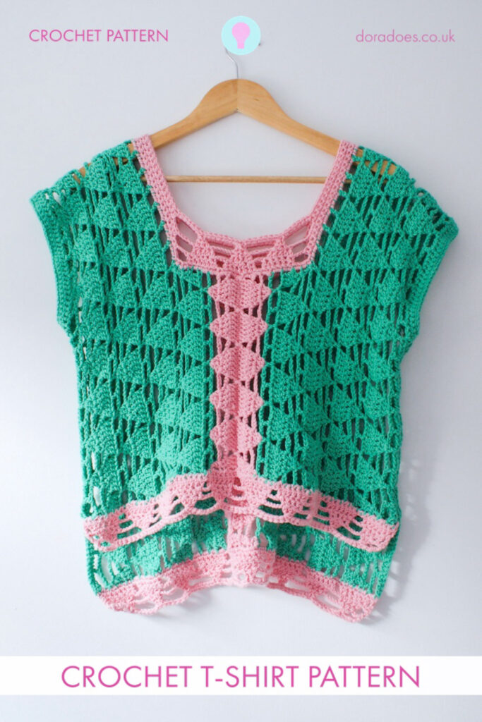 A green and pink lace crochet t-shirt with triangle motifs hands from a wooden hangar against a white wall. A text overlay reads ‘crochet t-shirt pattern.’