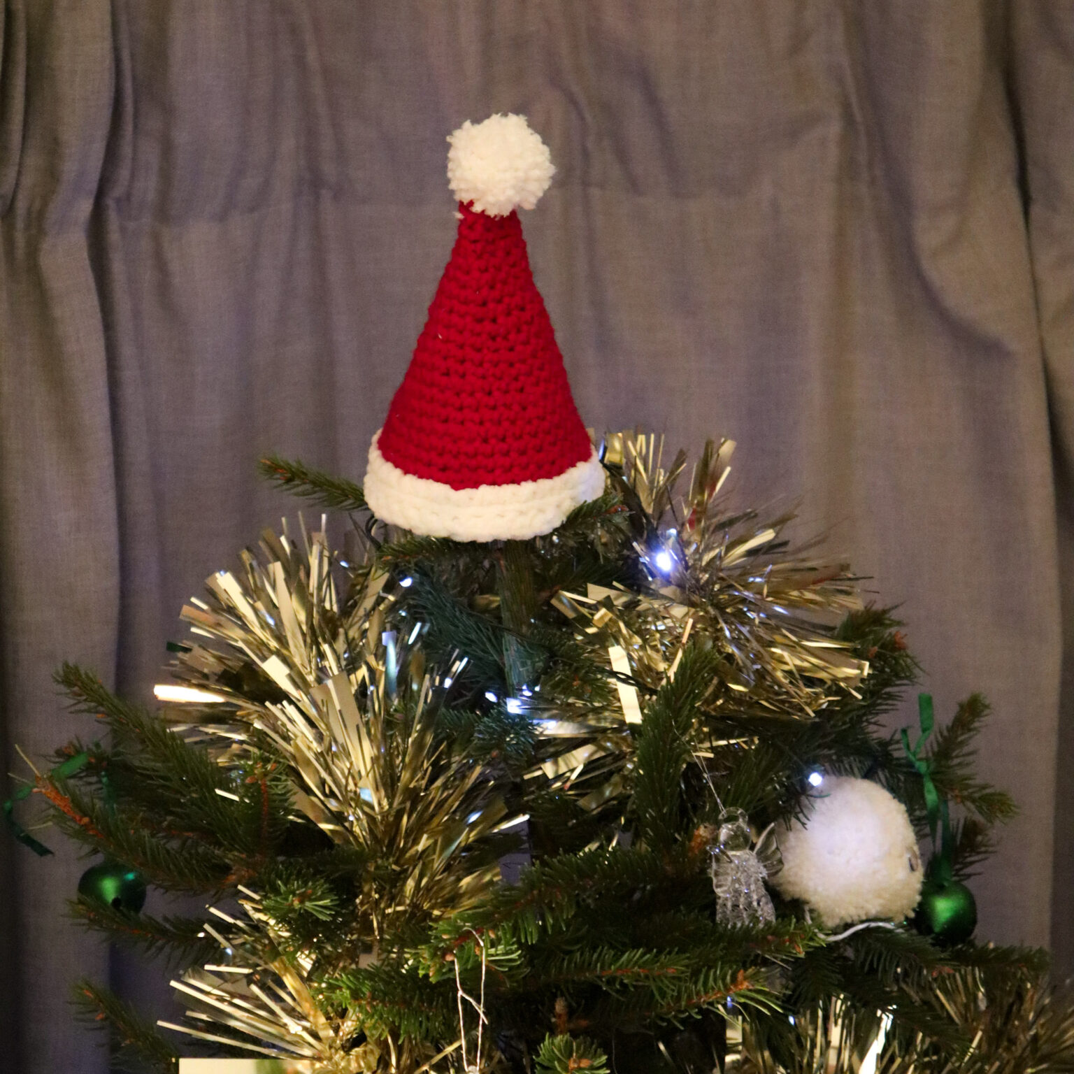 A close up of a crochet Santa Hat Christmas Tree topper.