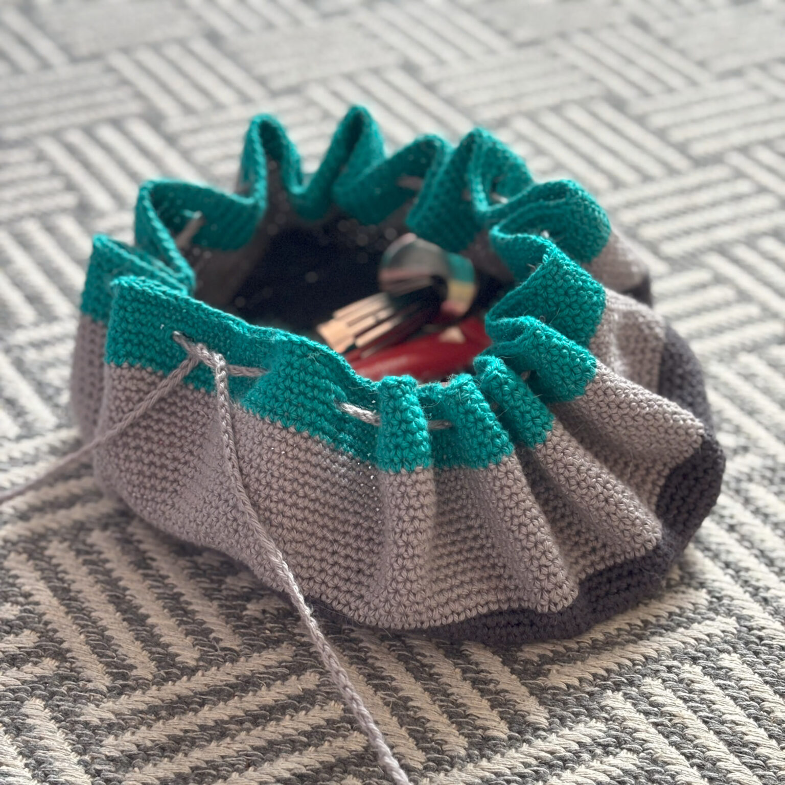 A drawstring crochet toiletry back is part closed revealing a few of the contents.