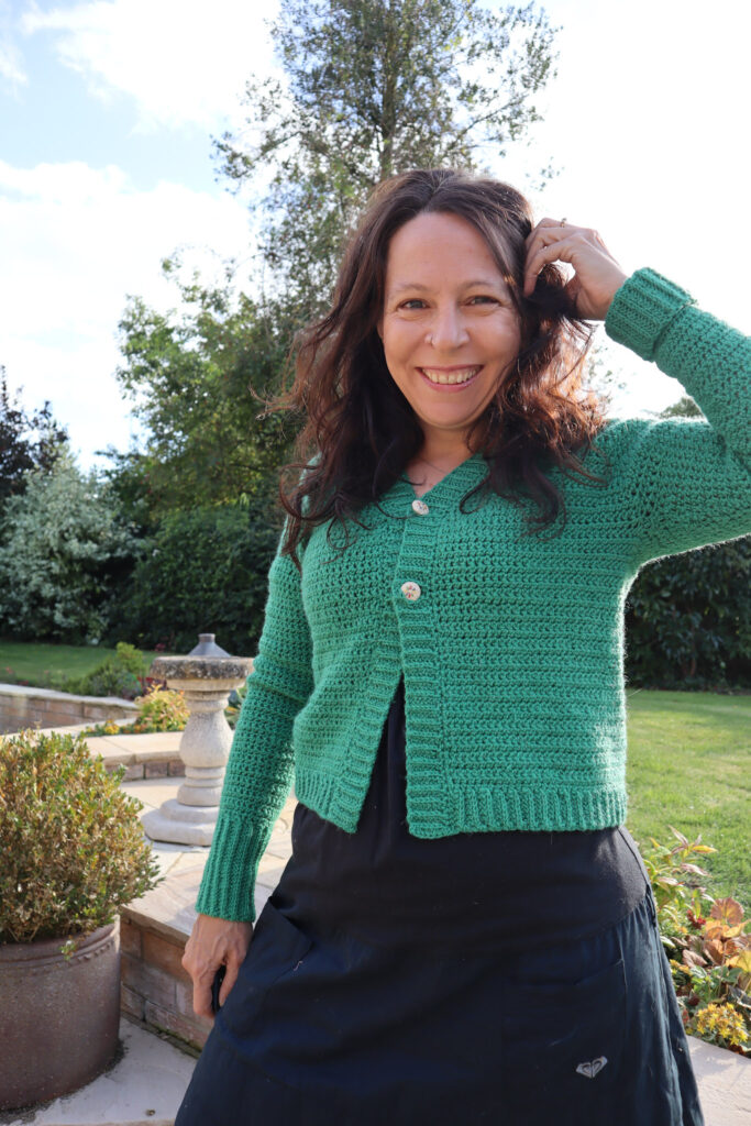 Dora wears a green double knit version of the any yarn will do crochet cardigan, a top down raglan seamless crochet cardigan.