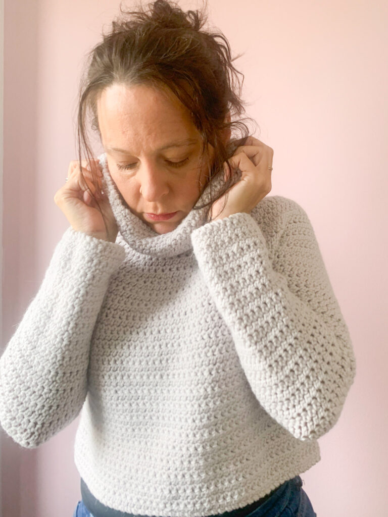 Dora wears a roll neck, cropped version of the any yarn will do crochet sweater made in aran weight natural cream yarn.