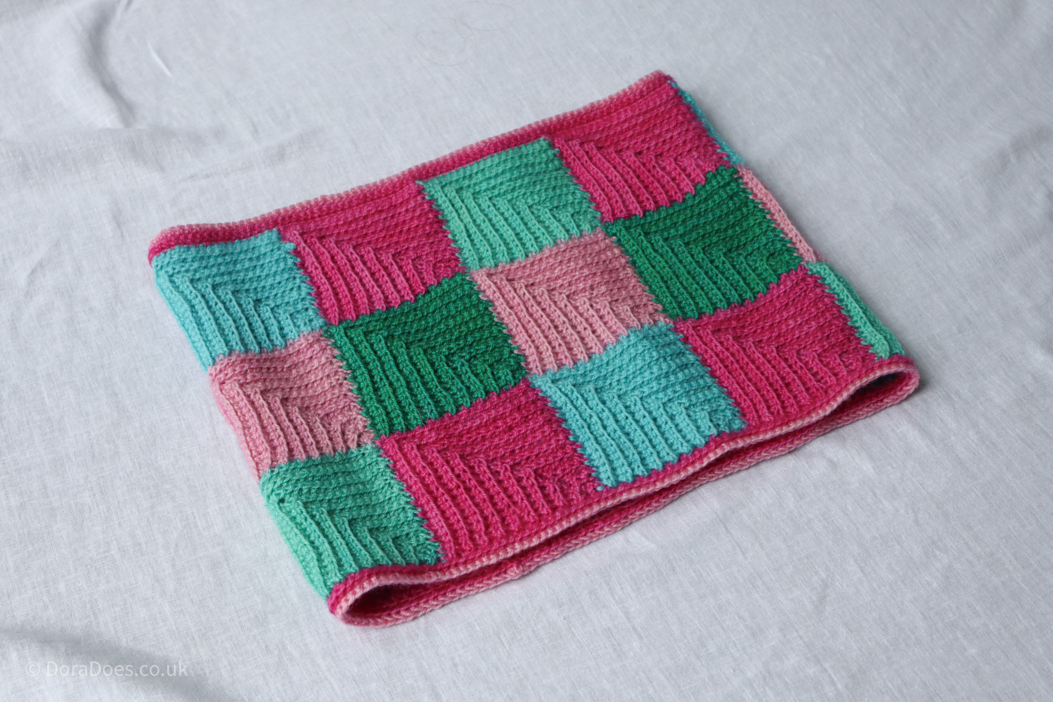 A crochet cowl made from mitred squares in shades of pink, green and turquoise.