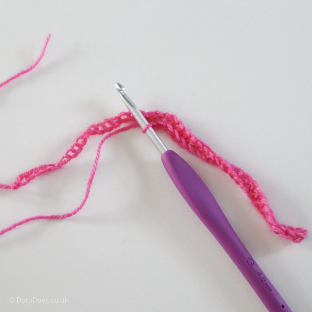 Crochet mitred square tutorial using pink yarn and a 4mm crochet hook, mid way through first proper row: Step 3.