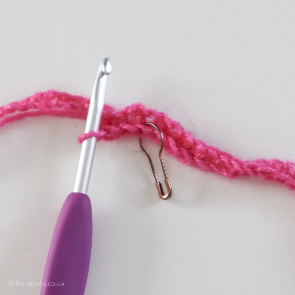 Crochet mitred square tutorial using pink yarn and a 4mm crochet hook. A close up of where the stitch marker is placed in the first row: Step 4.