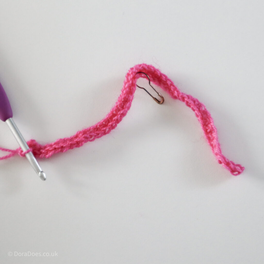 Crochet mitred square tutorial using pink yarn and a 4mm crochet hook and a stitch marker placed in the corner: Step 5.
