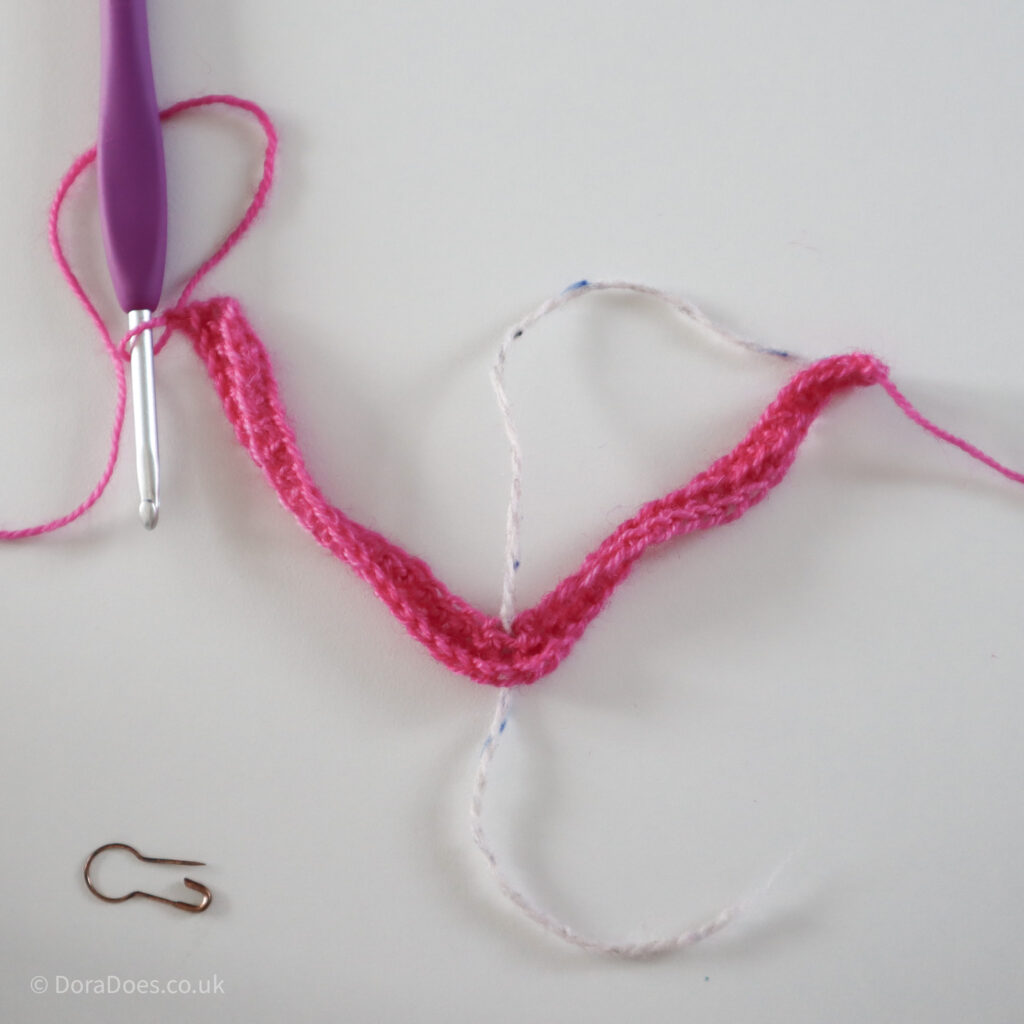 Crochet mitred square tutorial using pink yarn and a 4mm crochet hook shown after the first complete row where there is still a twist in the yarn: Step 6.
