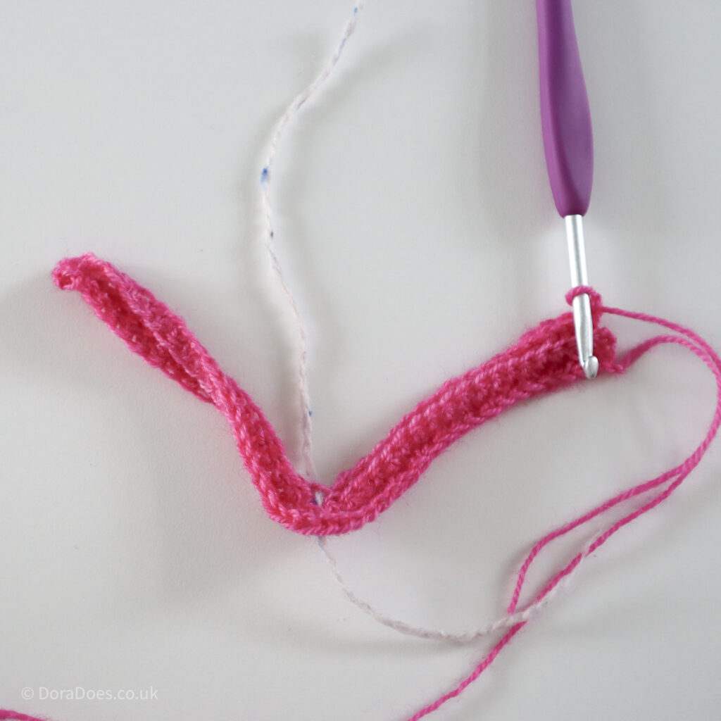 Crochet mitred square tutorial using pink yarn and a 4mm crochet hook and white running stitch marker after 3 rows: Step 7.