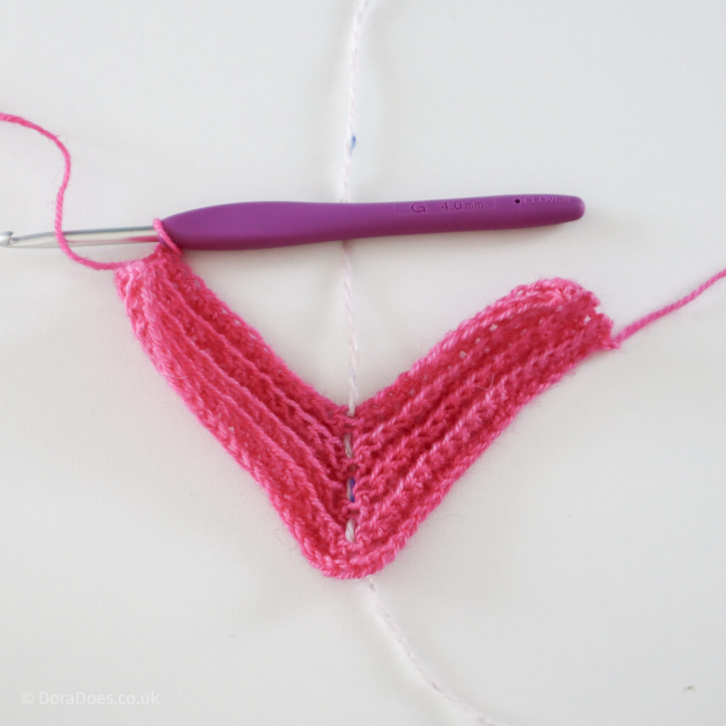 Crochet mitred square tutorial using pink yarn and a 4mm crochet hook, about a third of the way through: Step 10.
