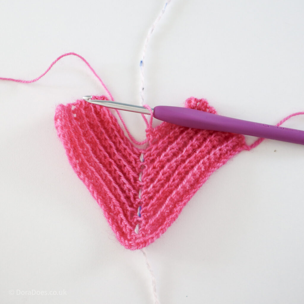 Crochet mitred square tutorial using pink yarn and a 4mm crochet hook, shown about two thirds through the square, half way through a row: Step 12.