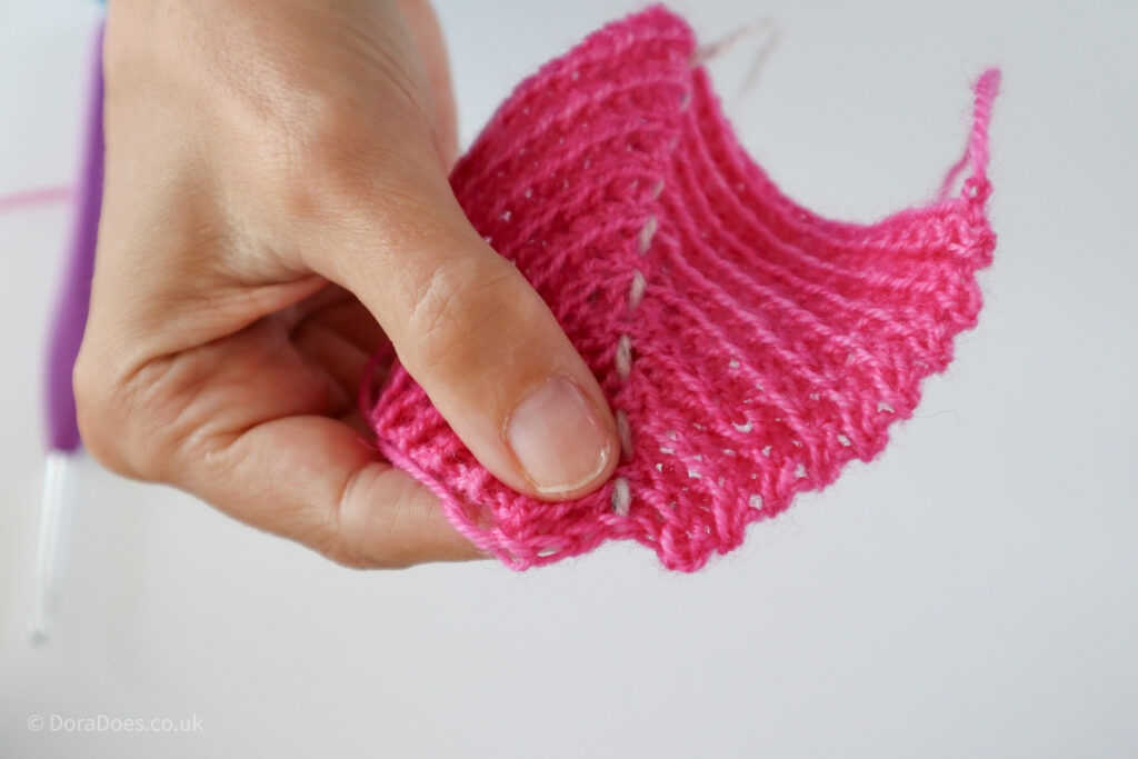 A close up of the penultimate row of a crochet mitred square being held with the short rows up front.