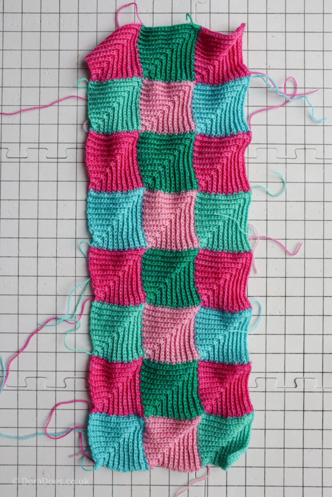 A crochet length of fabric made up of 24 mitred squares is seen in portrait from above on a blocking board.
