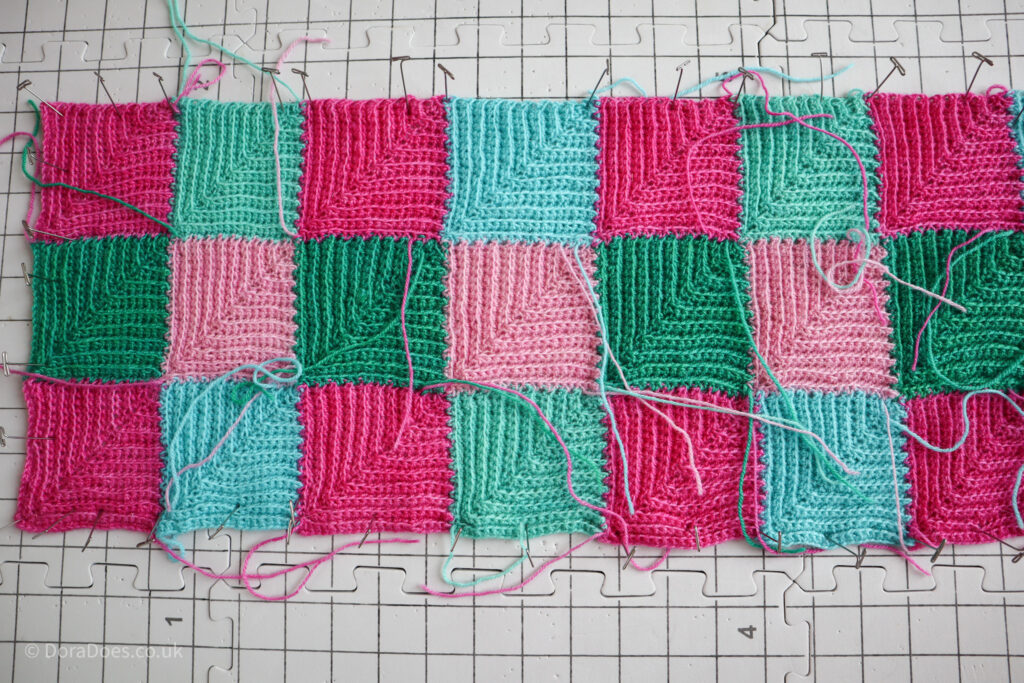A length of crocheted fabric made up of mitred squares pinned out to a blocking board.