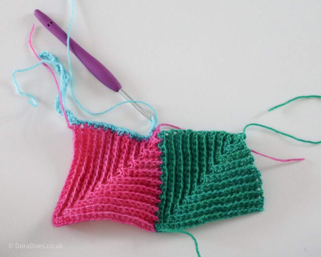 Two joined crochet mitred square with a third square in turquoise yarn in progress.