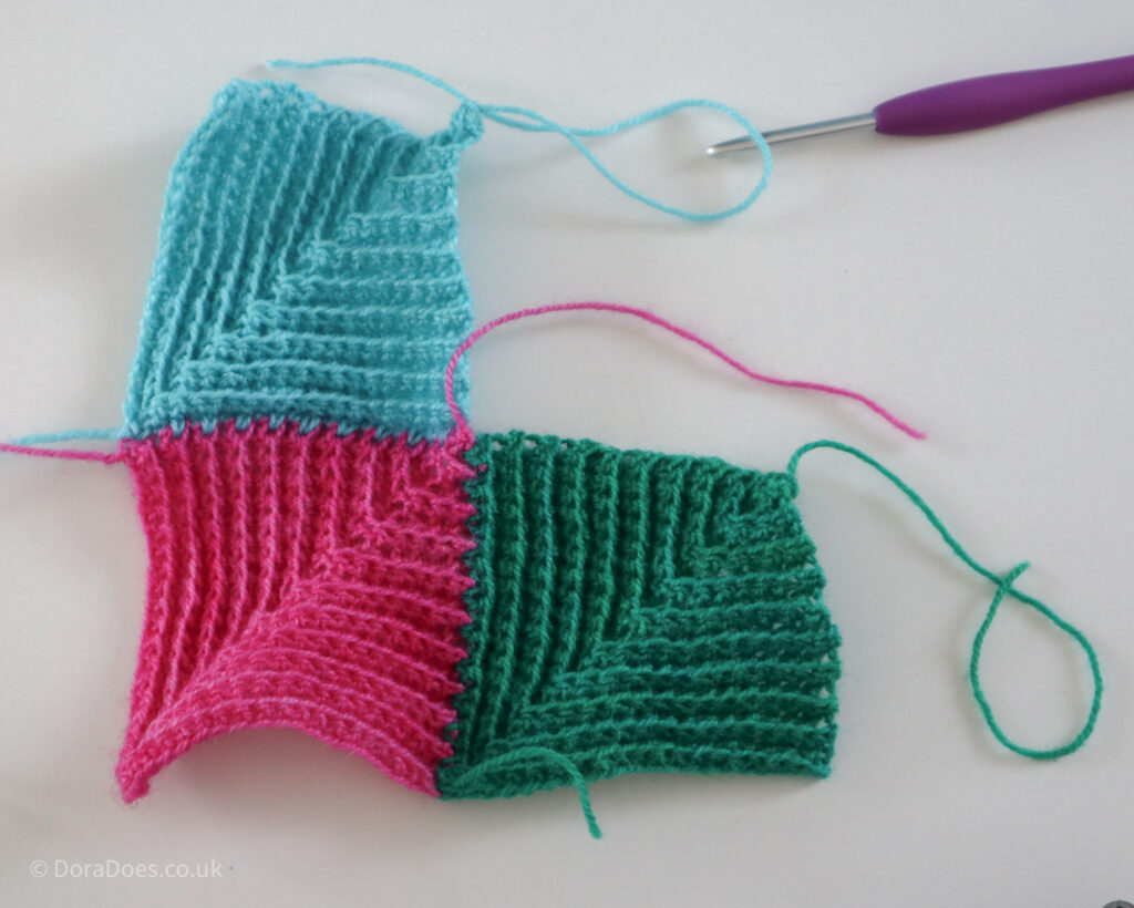 Three crochet mitred squares, a pink, green and turquoise one, with a purple crochet hook laying beside them, The squares were joined using the jayg method.