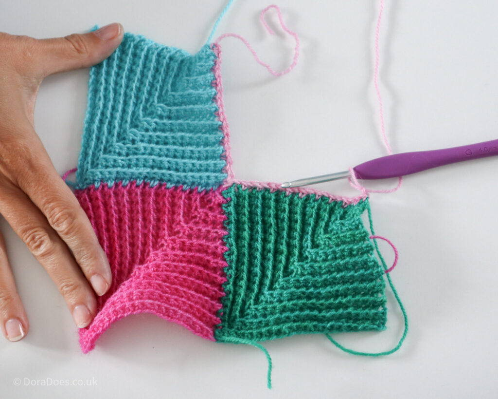 The first row of a fourth pink crochet mitred square, joined to two other squares to create a group of 4.