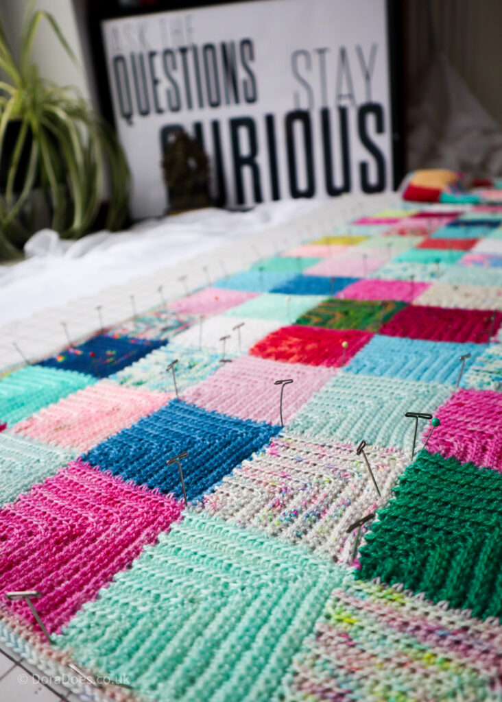 A close up of a crochet patchwork mitred squares wrap pinned out on a blocking board.