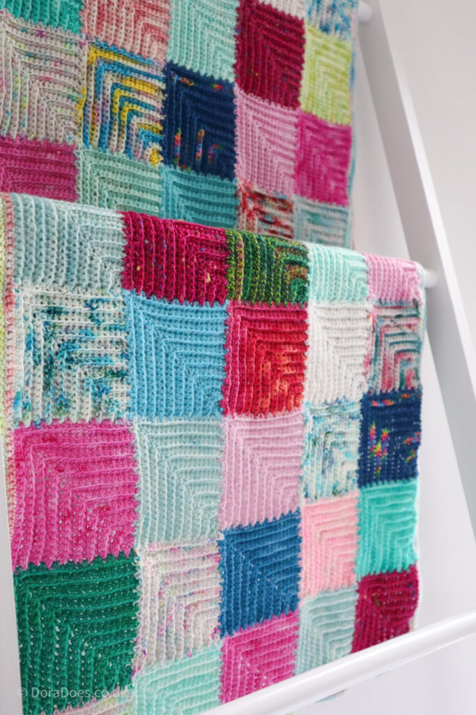 A close up of the mitred minis crochet wrap draped over a blanket ladder.
