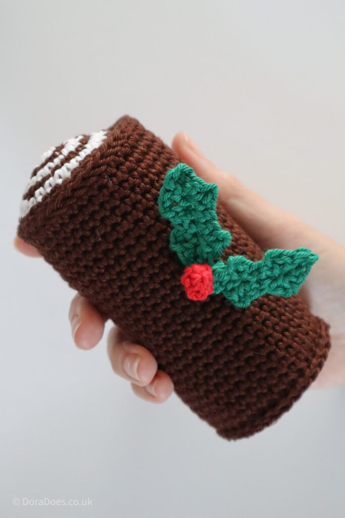 A portrait view of a finished crochet Yule log with holly leaf embelishment.