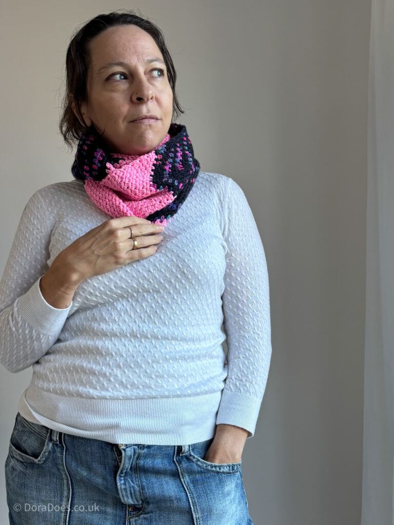 Dora wears a small, bright coloured infinity scarf crocheted with bright contrasting double knit yarn and paired with a lightweight cream sweater.