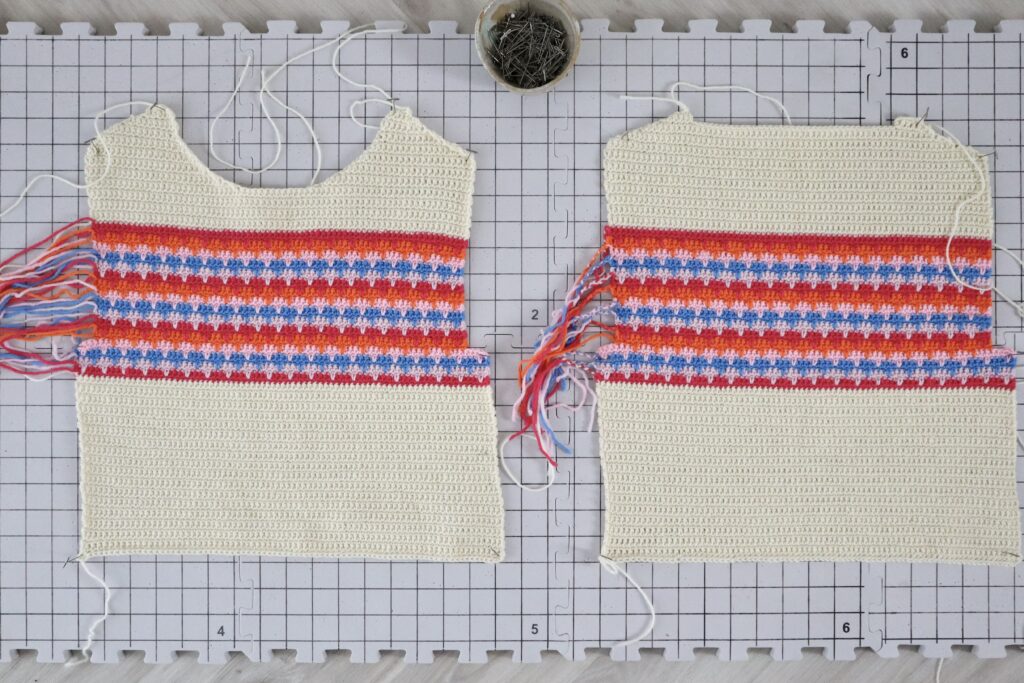 To crochet garment panels are gently pinned out on a blocking board. The piece on the left had a rounded neckline with sloping shoulders and will become the front of the sweater. The crochet panel on the left has a shallow neck drop and will become the back of the sweater.