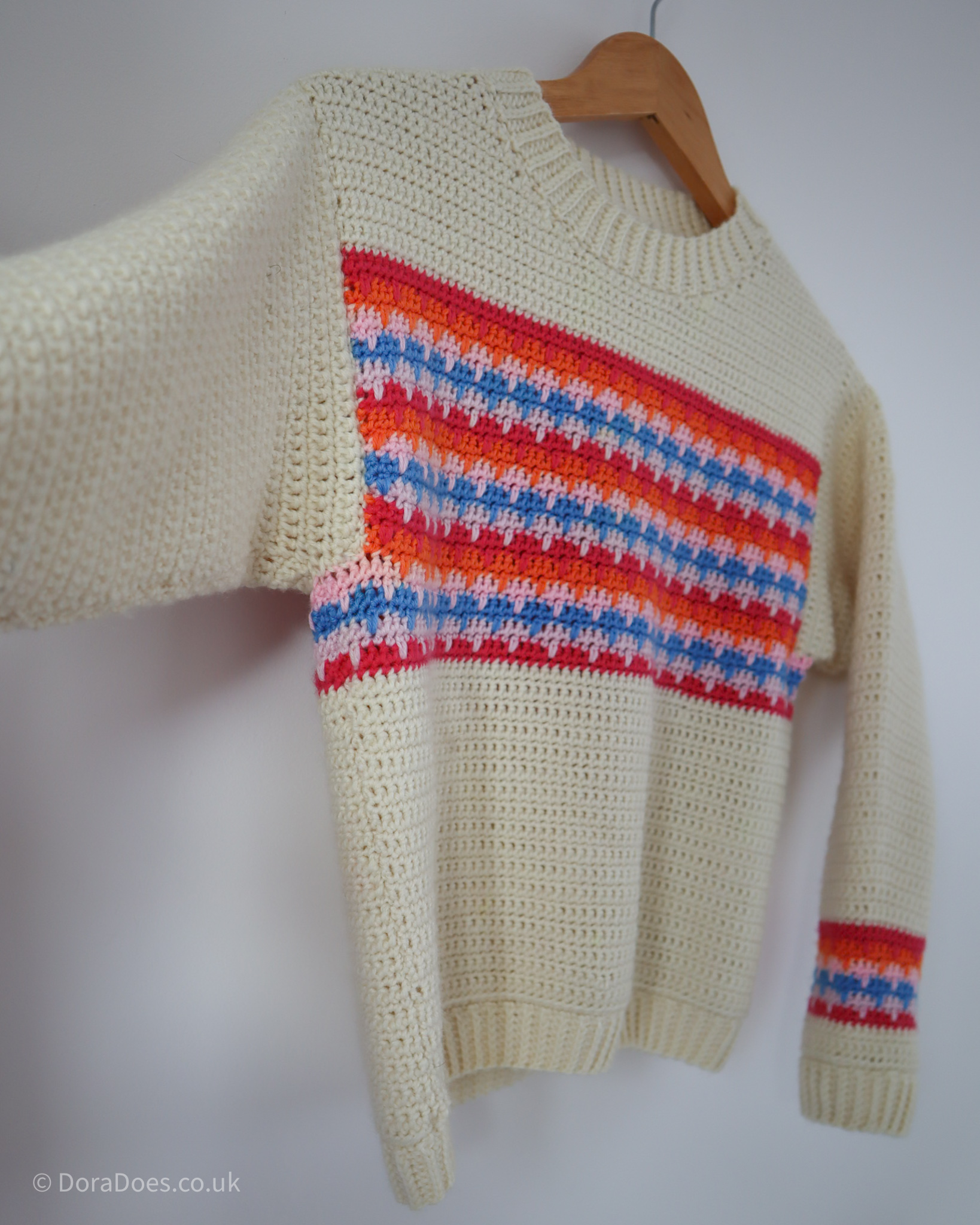 A close up of the Lark Sweater pattern sample. A fitted crochet sweater made from undyed natural wool double knit harness with bright colourful stripes over the chest and wrists. The colour work uses a modified larks foot crochet stitch.